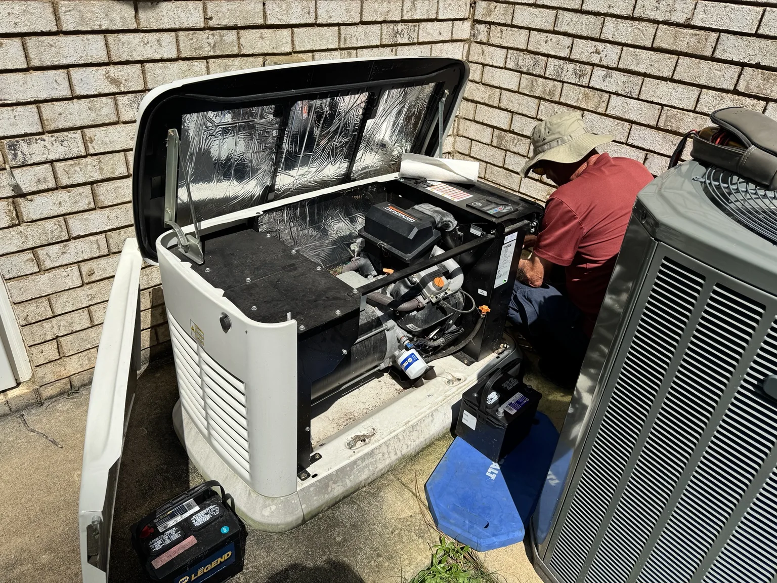 Technician servicing a Generac home standby generator beside a brick home